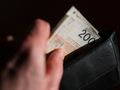Na zdjęciu widać rękę wyjmującą banknot 200 zł z czarnego portfela.