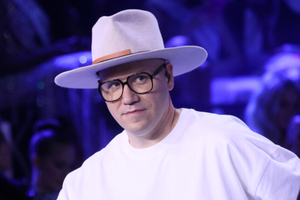 Gromee w jasnym kapeluszu i okularach, w białej koszulce, na tle ciemnej sceny.