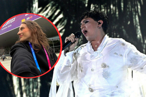 Kobieta w czarnej bluzie z identyfikatorem, obok artysta w białej kreacji śpiewający na scenie.