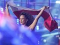 Kobieta z kręconymi włosami trzyma flagę Polski na tle kolorowych świateł.
