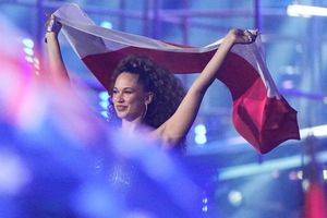 Kobieta z kręconymi włosami trzyma flagę Polski na tle kolorowych świateł.