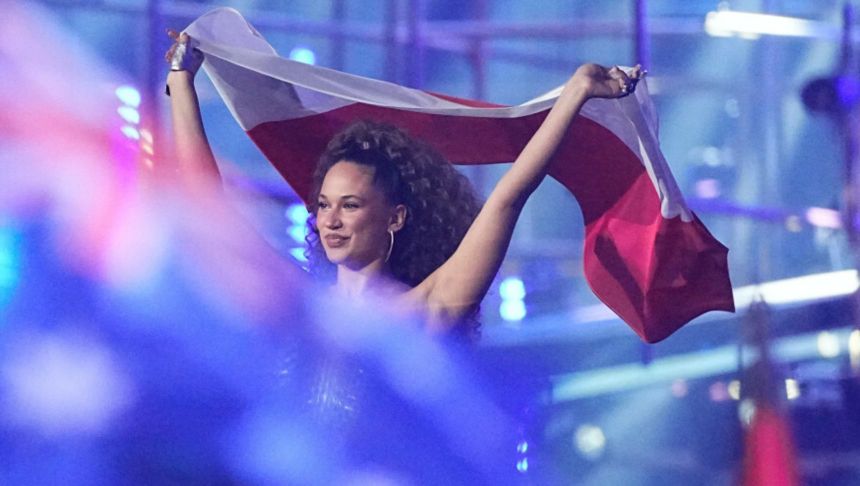 Kobieta z kręconymi włosami trzyma flagę Polski na tle kolorowych świateł.