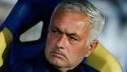 Jose Mourinho siedzi na ławce, z poważnym wyrazem twarzy, w sportowej odzieży.