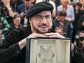 Mężczyzna w beretach uśmiecha się, trzymając nagrodę. W tle grupka fotografów.