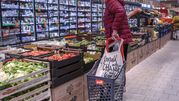 Kobieta w czerwonej kurtce przy stoisku z warzywami w supermarkecie, obok wózek na zakupy.