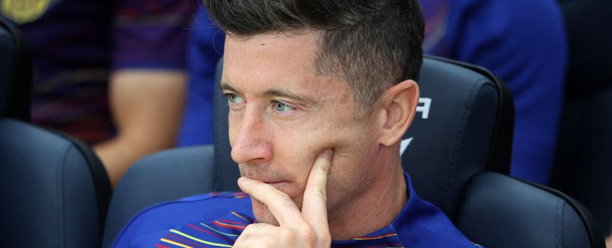 Na zdjęciu Robert Lewandowski, myślący, siedzi na ławce drużynowej w niebieskiej koszulce FC Barcelony.