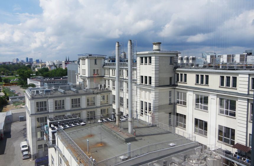Widok na nowoczesny budynek przemysłowy z kominami i zielonym otoczeniem w tle.
