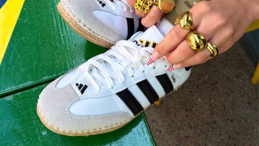 Zdjęcie białych butów Adidas z czarnymi paskami, ręka z ozdobnymi pierścionkami.