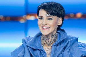 Na zdjęciu uśmiechnięta kobieta w niebieskiej bluzie, z tatuażami na szyi i dekolcie.