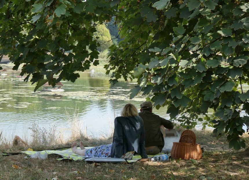 Para siedzi nad jeziorem, otoczona drzewami, relaksując się na kocu i podziwiając widok.