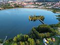 Widok na jezioro otoczone zielenią, z plażą i atrakcjami dla dzieci w tle.