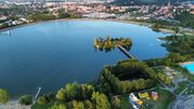 Widok na jezioro otoczone zielenią, z plażą i atrakcjami dla dzieci w tle.