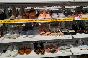 Na zdjęciu półki z różnorodnymi obuwiem na wyprzedaży, w tym sandały i sneakersy.