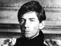 Ian McKellen w ciemnym stroju, poważny wyraz twarzy, klasyczne tło. Portret w czerni i bieli.
