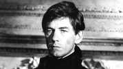 Ian McKellen w ciemnym stroju, poważny wyraz twarzy, klasyczne tło. Portret w czerni i bieli.