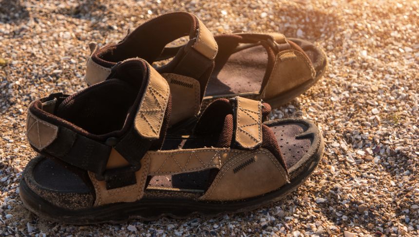 Sandały na tle plaży, z piaskiem i muszelkami wokół. Ciepłe, letnie światło zachodu słońca.