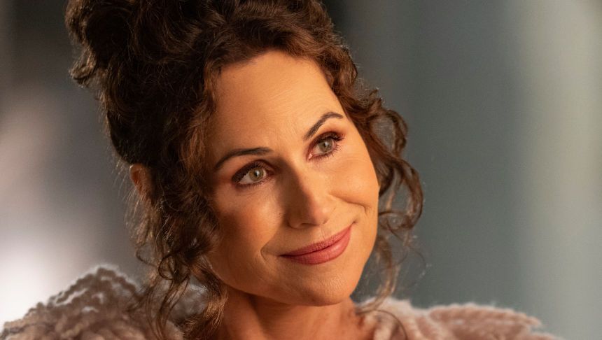 Kobieta z kręconymi włosami, uśmiechająca się, w jasnym ubraniu.