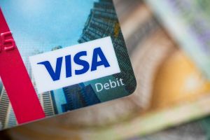 Zdjęcie karty debetowej Visa na tle banknotów. Widoczne logo Visa w kolorze niebieskim.