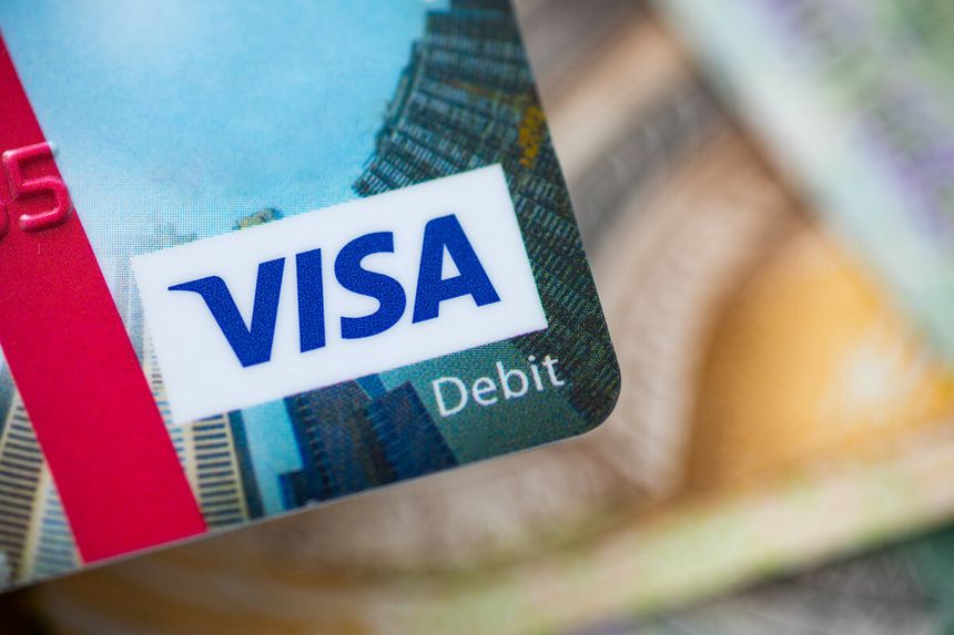 Zdjęcie karty debetowej Visa na tle banknotów. Widoczne logo Visa w kolorze niebieskim.