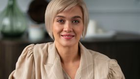 Kobieta z krótkimi blond włosami w jasnej bluzie, uśmiechająca się do aparatu.