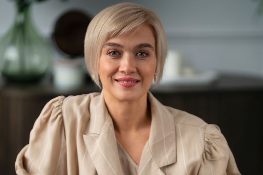Kobieta z krótkimi blond włosami w jasnej bluzie, uśmiechająca się do aparatu.