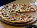 Pizza z pepperoni, oliwkami i papryką, część już pokrojona, podana na drewnianym talerzu.