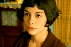 Audrey Tautou z krótkimi, ciemnymi włosami, patrząca w stronę obiektywu, w tle jasne wnętrze.