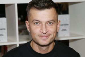 Osoba z krótkimi włosami, uśmiechająca się, w czarnej koszulce, w tle białe książki.