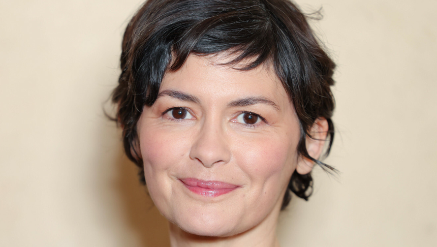 Na zdjęciu uśmiechnięta Audrey Tautou z krótkimi, ciemnymi włosami na neutralnym tle.