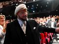 Mężczyzna w białym kapeluszu wita się z publicznością w tle stoją ludzie w formalnym ubiorze.