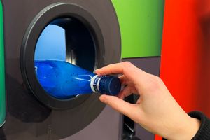 Osoba wrzuca niebieską butelkę do otworu recyklingowego maszyny. Tło w różnych kolorach.