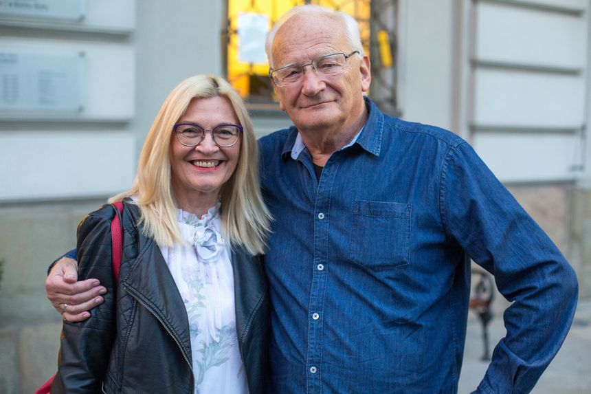 Na zdjęciu uśmiechnięta para w casualowych ubraniach, pozująca na zewnątrz budynku.