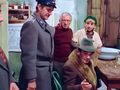 Grupa osób w wiejskiej chatce, przy stole, w scenie z filmu komediowego.