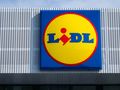 Znajduje się logo sklepu Lidl. Żółte kółko z niebieskim napisem na tle nieba.
