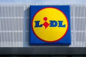 Znajduje się logo sklepu Lidl. Żółte kółko z niebieskim napisem na tle nieba.