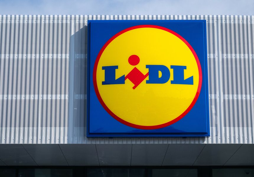 Znajduje się logo sklepu Lidl. Żółte kółko z niebieskim napisem na tle nieba.