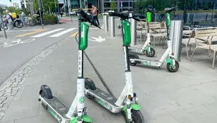 Zielone hulajnogi elektryczne stoją na chodniku, w tle rowery i budynki.