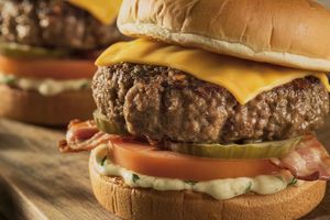 Zdjęcie przedstawia dwa soczyste burgery z serem, pomidorem, boczkiem i marynowanym ogórkiem.