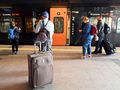 Grupa osób czeka przy pociągu z bagażami na stacji. W tle widoczne informacje o trasach.