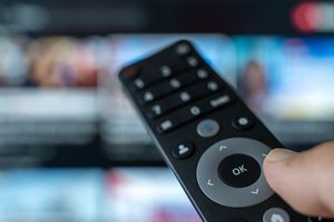 Pilot do telewizora trzymany w dłoni, w tle rozmyte menu telewizyjne
