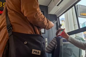 Osoby w autobusie, jedna skanuje bilet telefonem, druga trzyma telefon z kodem QR.