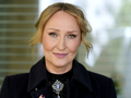 Anita Lipnicka w czarnym płaszczu, z uśmiechem, stojąca na tle rozmytej przestrzeni.
