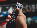Ręka trzymająca pilot do telewizora, w tle zarysy ekranów z serialami animowanymi.