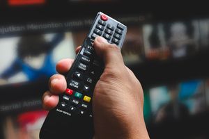 Ręka trzymająca pilot do telewizora, w tle zarysy ekranów z serialami animowanymi.