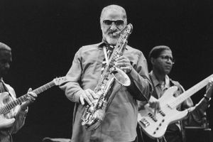 Muzycy jazzowi na scenie; mężczyzna gra na saksofonie, w tle gitarzysta i basista.