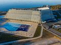 Nowoczesny budynek hotelu z basenem, otoczony terenami zielonymi i wodami. Czyste niebo w tle.
