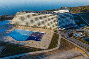 Nowoczesny budynek hotelu z basenem, otoczony terenami zielonymi i wodami. Czyste niebo w tle.