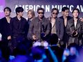 Czterech mężczyzn stoi na scenie w eleganckich strojach, trzymając nagrodę, w tle napisy AMERICAN MUSIC AWARDS.