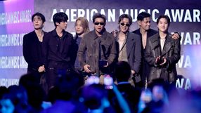 Czterech mężczyzn stoi na scenie w eleganckich strojach, trzymając nagrodę, w tle napisy AMERICAN MUSIC AWARDS.