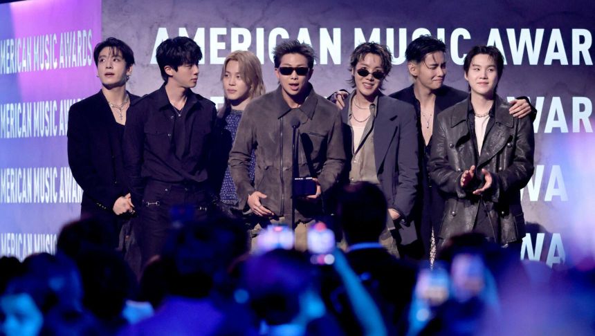 Czterech mężczyzn stoi na scenie w eleganckich strojach, trzymając nagrodę, w tle napisy AMERICAN MUSIC AWARDS.